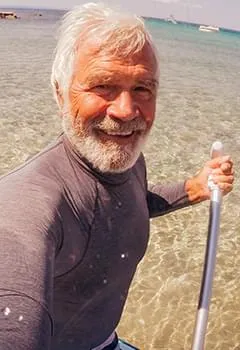 Happy senior active man holding a water paddle at the beach, showcasing physical stamina and robust cardiovascular health.